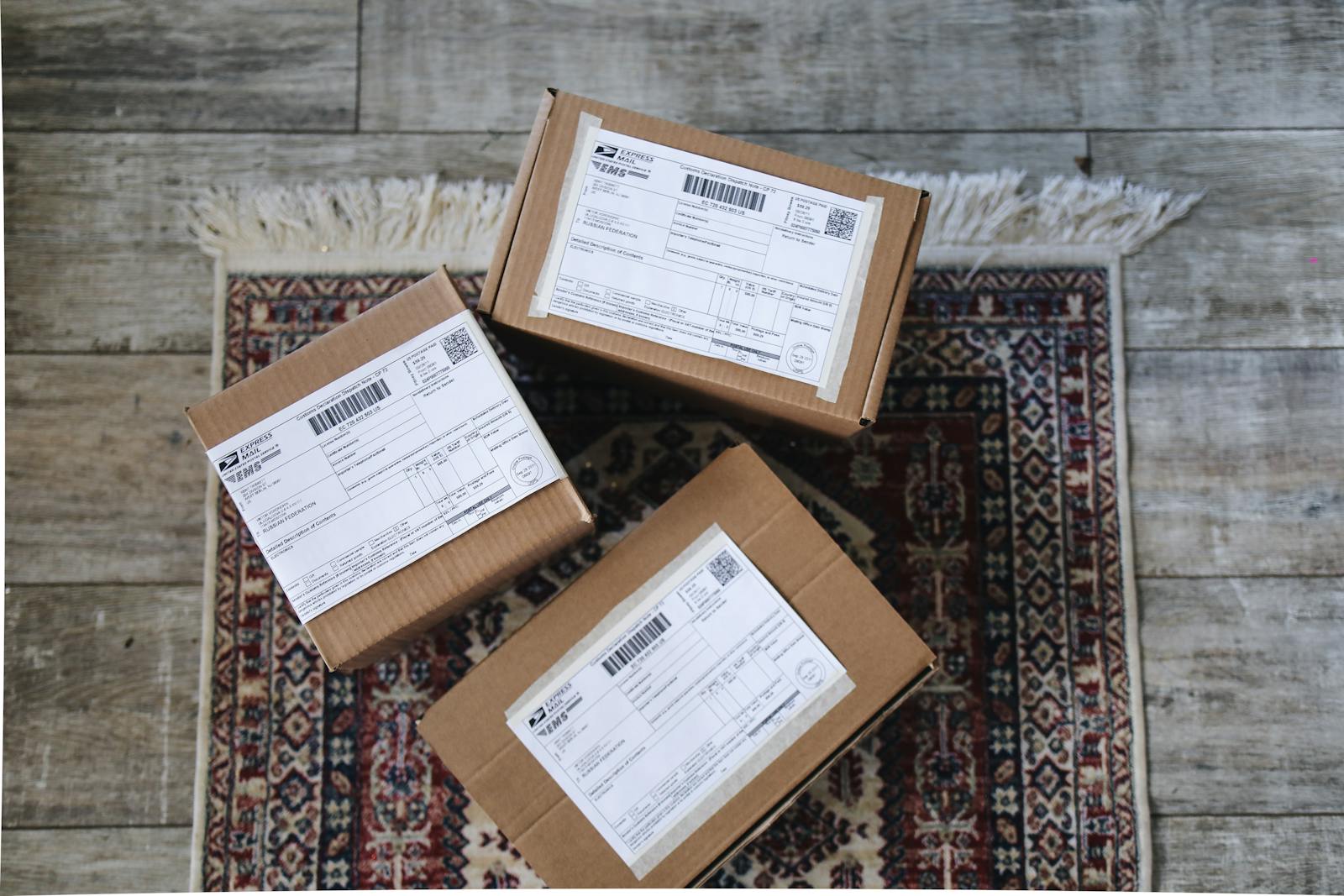 Three labeled delivery boxes placed on a decorative rug over a wooden floor.